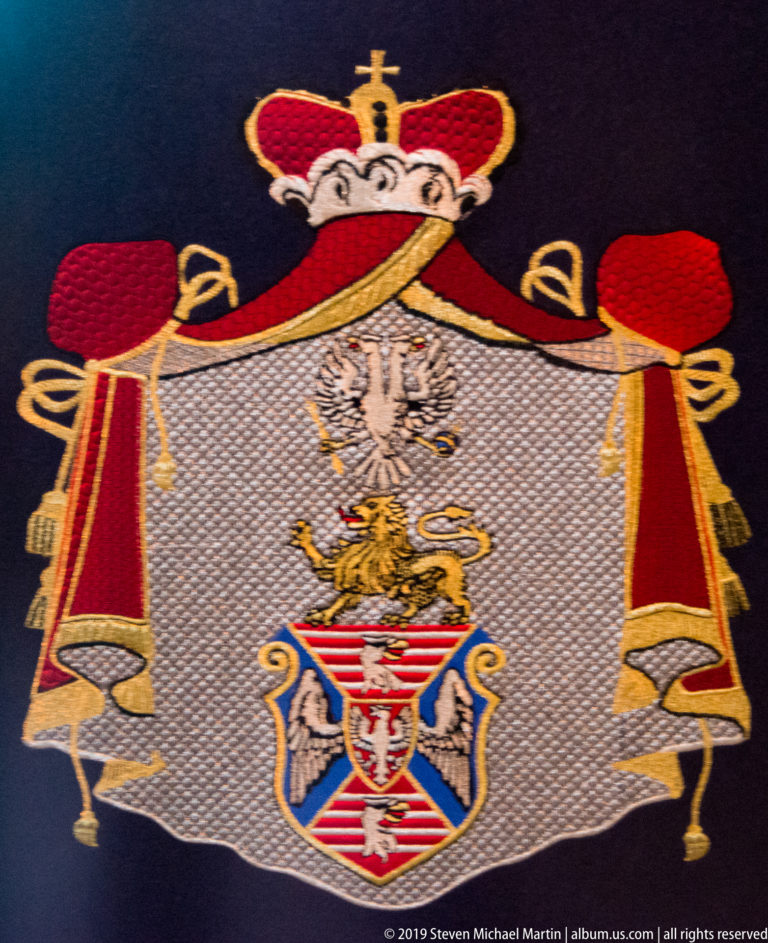 Close view of an embroidered heraldic emblem with a double-headed eagle, shield motifs, and red-and-gold ceremonial decoration.