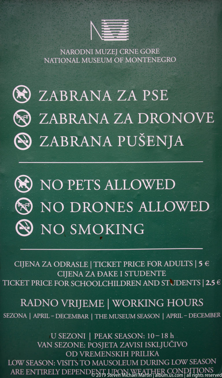 Green National Museum of Montenegro sign listing no pets, no drones, no smoking, ticket prices, and working hours.