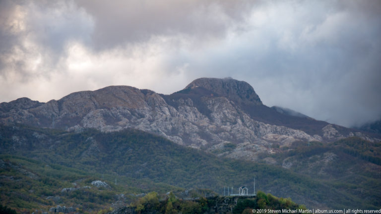 Gray limestone ridge above forested slopes beneath dark storm clouds in the Lovćen mountains.