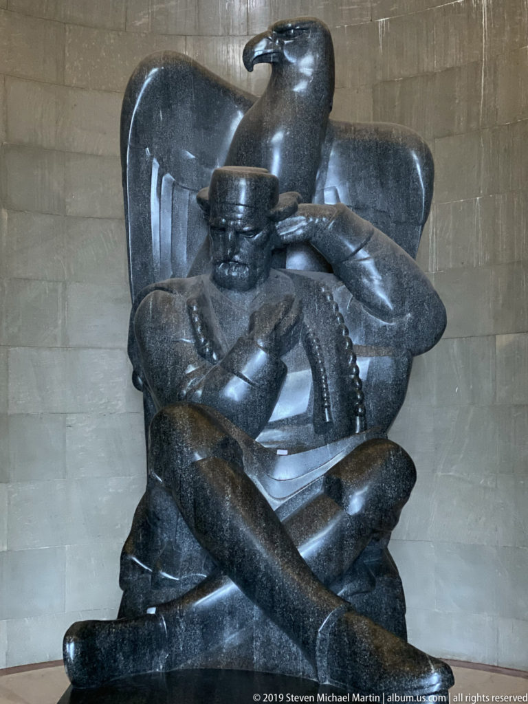 Close frontal view of the dark seated statue of Petar II Petrović-Njegoš with a large stylized eagle behind him.