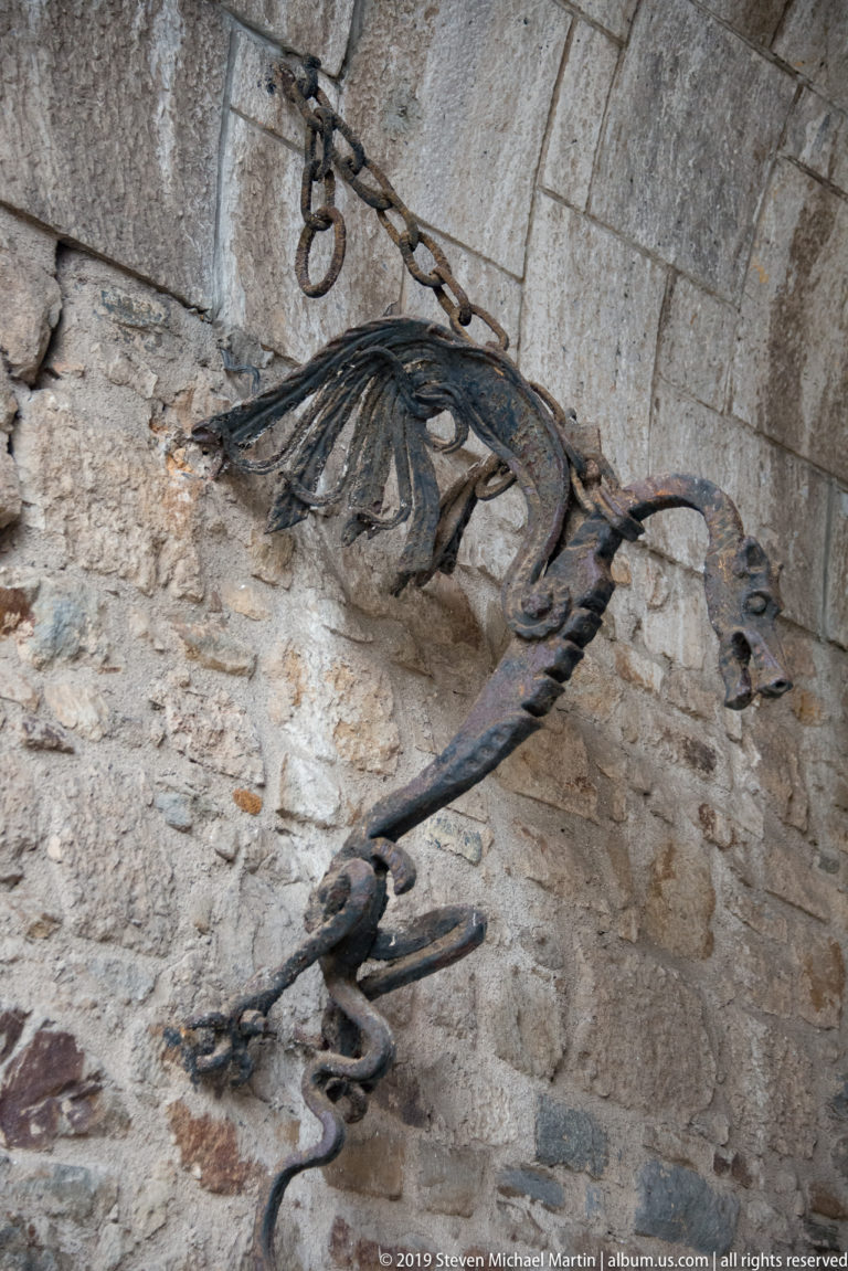 Forged-metal dragon sculpture attached to a stone wall at Ljubljana Castle, with spread wings and a curled tail.