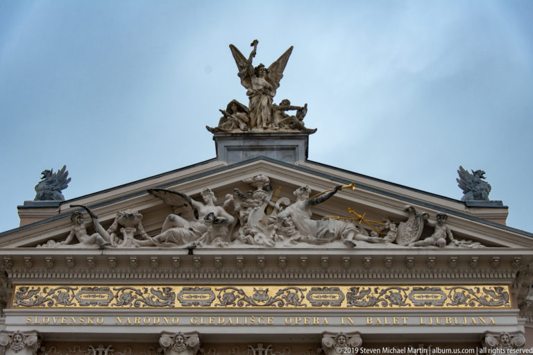 Figural pediment, gilded frieze, and roof sculpture above the Slovenian National Opera and Ballet inscription.