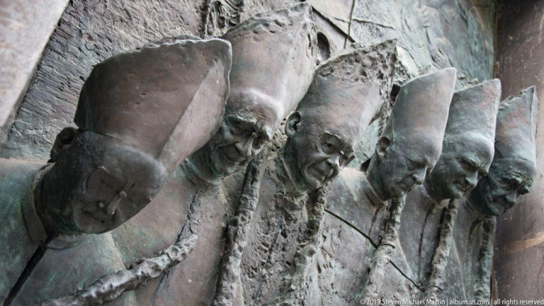 Close view of mitred bishops modeled in high relief on the bronze doors of Ljubljana Cathedral.