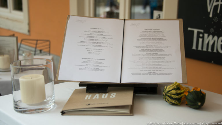 Open restaurant menu on a stand beside a glass candle holder and small decorative gourds.