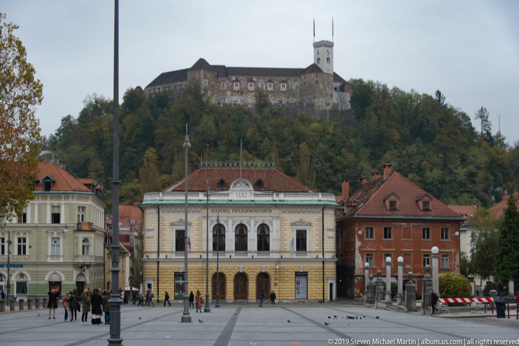 Slovenian Philharmonic building in the foreground with Ljubljana Castle rising on the wooded hill behind.