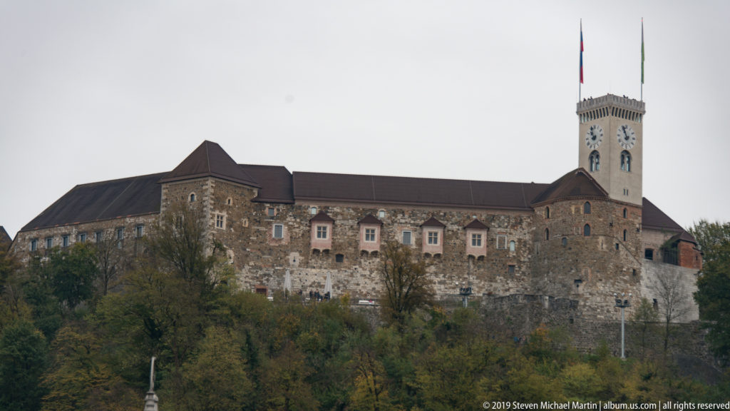 Ljubljana Castle with its clock tower and long stone walls rising above wooded Castle Hill.