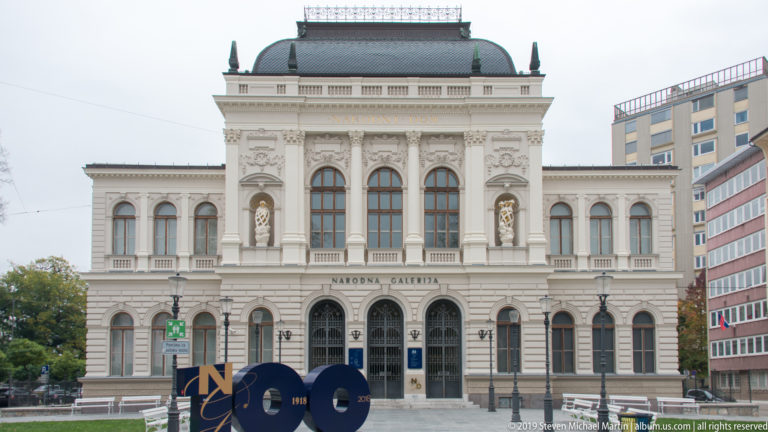 Frontal view of Slovenia’s National Gallery with arched windows, sculptural niches, mansard roof, and central entrance.