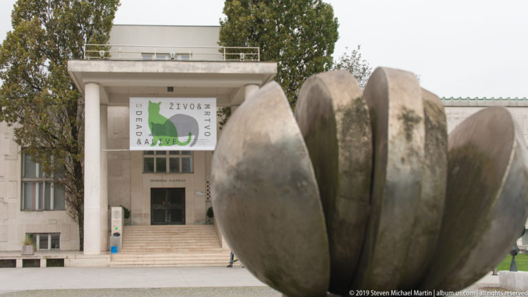 Large abstract sculpture in front of the stone entrance façade of Ljubljana’s Moderna galerija.