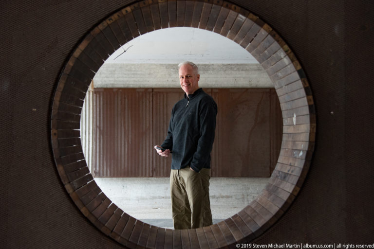 Man standing inside a large circular brick-framed opening in a modern architectural setting.