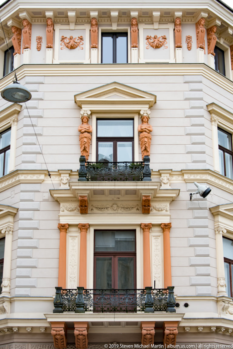 Two windows framed by terracotta-colored sculpted ornament, pilasters, brackets, and a triangular pediment.