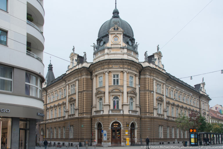 Full corner view of an ornate historic building with a central dome, long wings, and sculpted roofline.