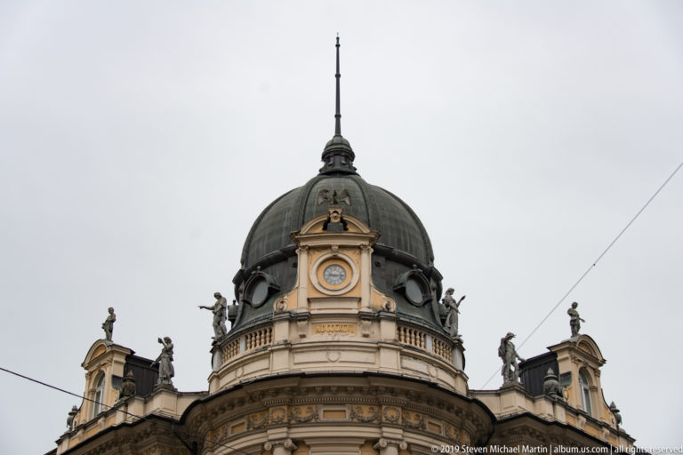 Close view of an ornate domed roof with central medallion, balustrade, and sculpted figures.
