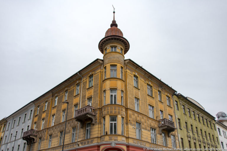 Yellow historic corner building with balconies, bay windows, and a tall cylindrical turret.