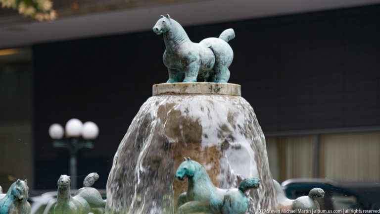 Bronze horse figures around a fountain, with one horse standing above a water-covered central pedestal.