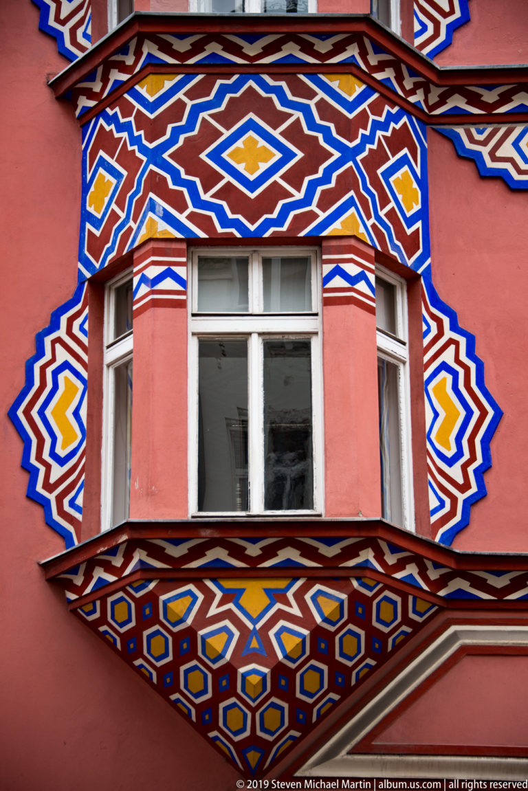 Close view of Vurnik House with bright geometric painted patterns surrounding windows on a pink façade.