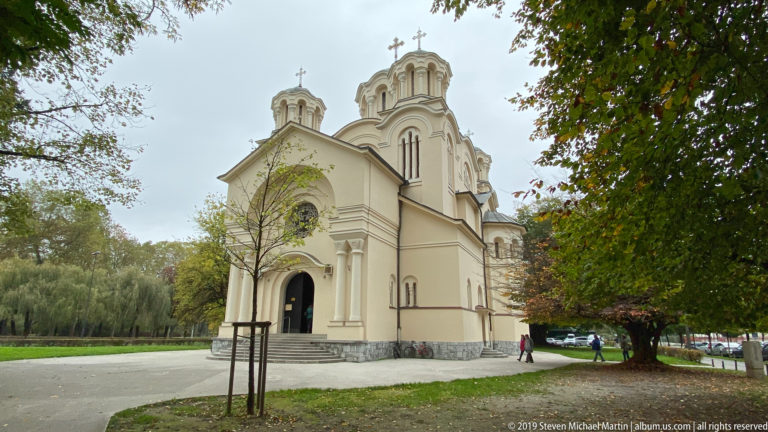Church of Saints Cyril and Methodius with cream walls and rounded towers standing among trees beside a park path.