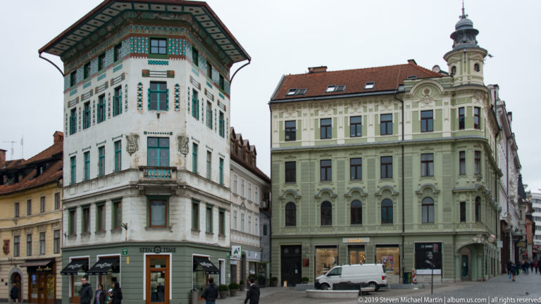 Two ornate historic corner buildings with decorative façades, green shutters, and a slender tower.