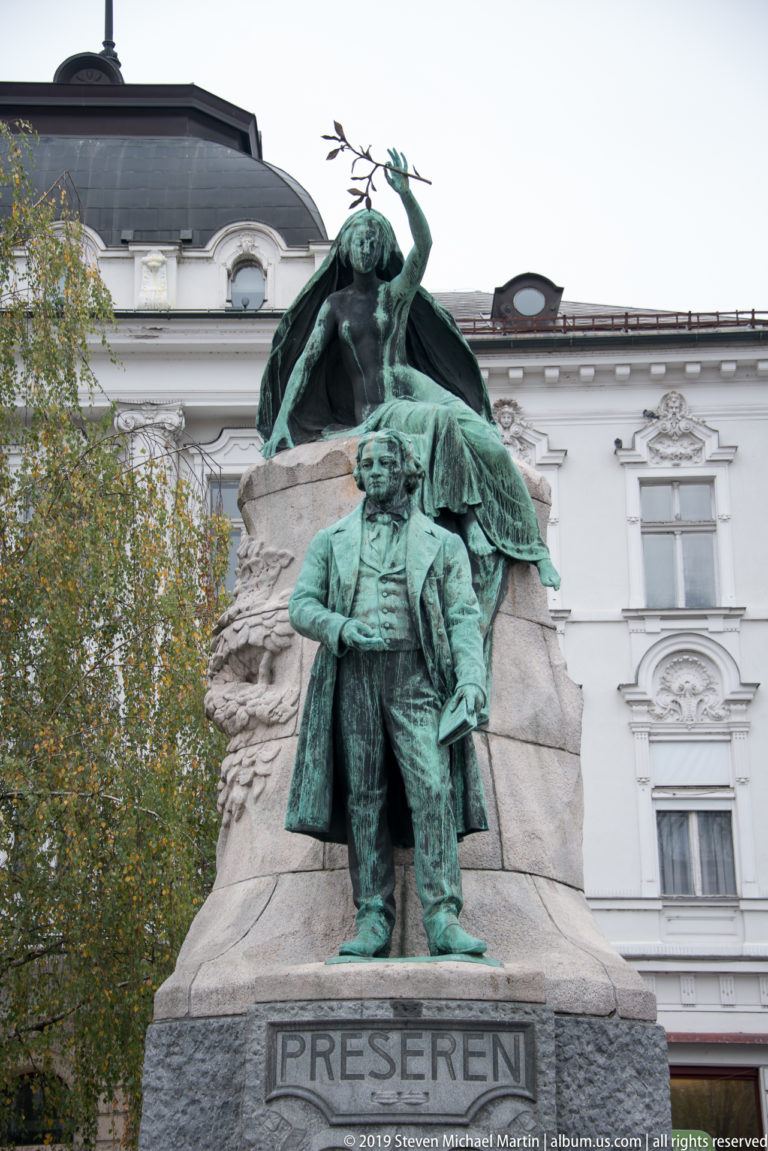 Bronze statue of France Prešeren with a female muse holding a laurel branch above him.