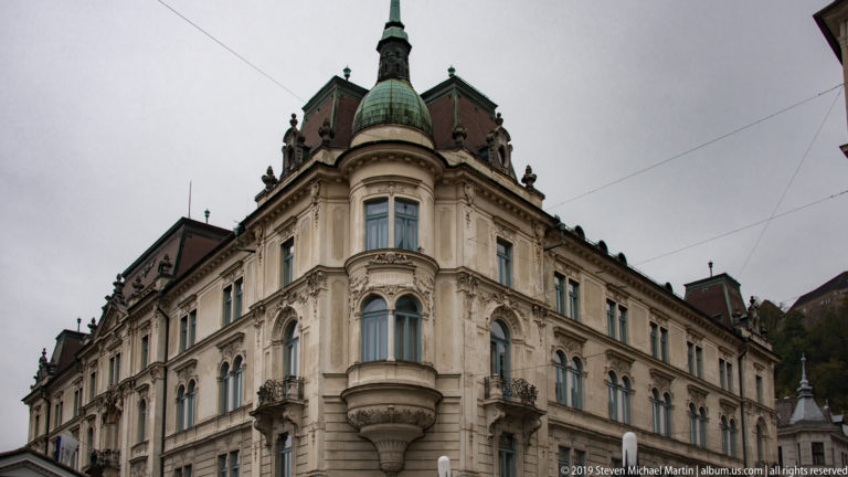 Ornate historic corner building with rounded bays, carved decoration, and a green domed turret.