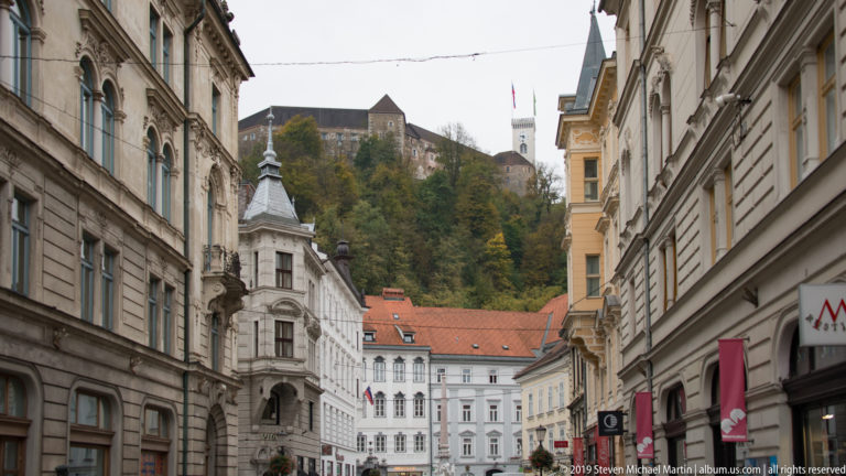 Historic Ljubljana street leading toward Ljubljana Castle on the wooded hill above.