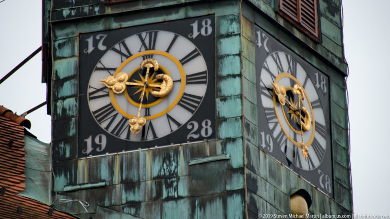 Two Roman-numeral clock faces with gilded hands on the green copper tower of Ljubljana Town Hall.