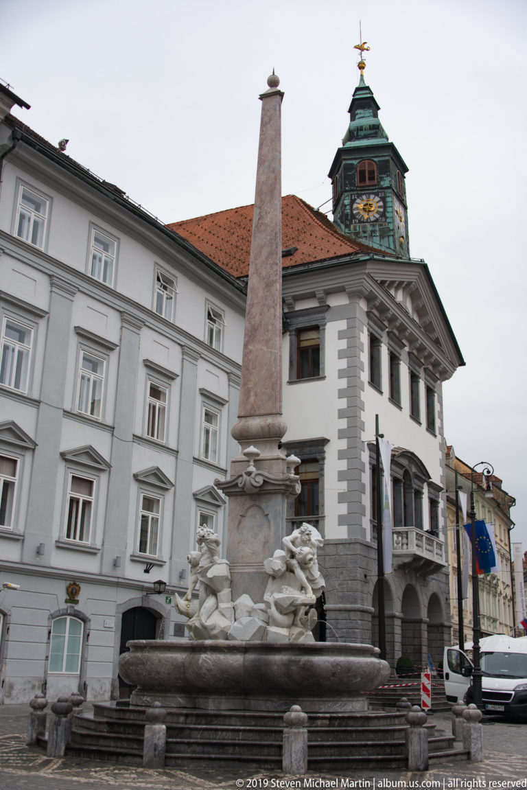 Robba Fountain with tall obelisk in front of Ljubljana Town Hall and its clock tower.
