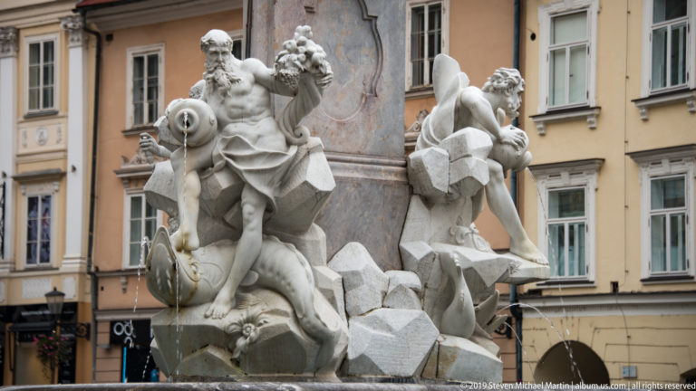 Close view of a muscular stone figure with a water vessel on the Robba Fountain in Ljubljana.