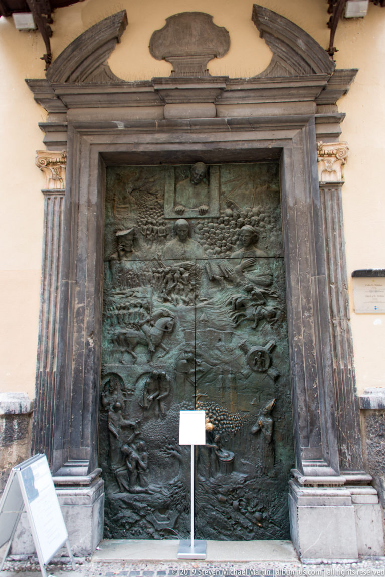 Large bronze relief door set in a dark stone frame at Ljubljana Cathedral.