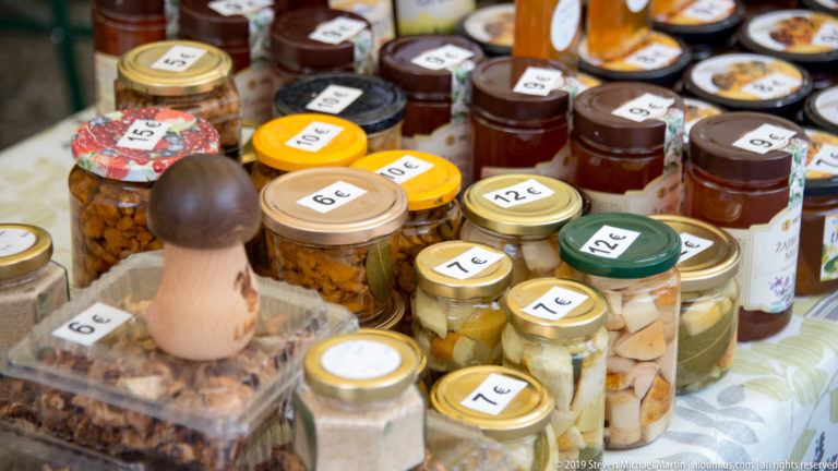 Rows of small priced jars beside a mushroom on an outdoor market table.