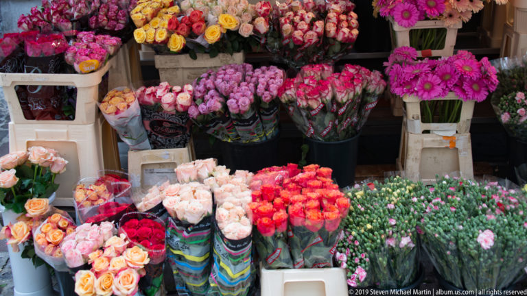 Outdoor flower stall packed with roses and mixed bouquets in pink, red, cream, orange, and purple.