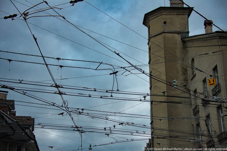 Tall historic masonry tower seen through a dense network of trolley wires.