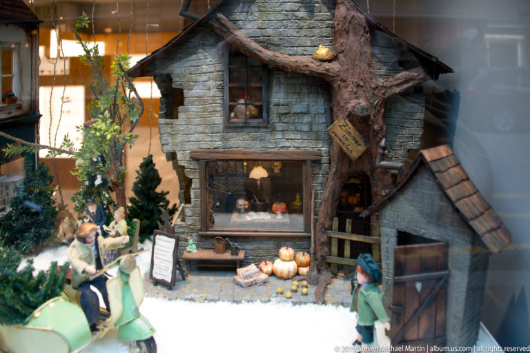 Miniature house, tree, figures, pumpkins and artificial snow in a shop-window display.