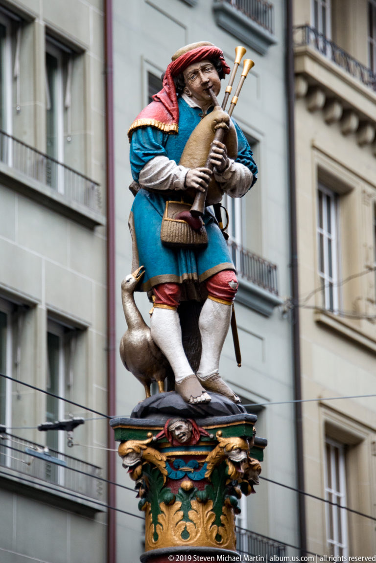 Painted bagpiper fountain figure in blue and red with a bird at his side.