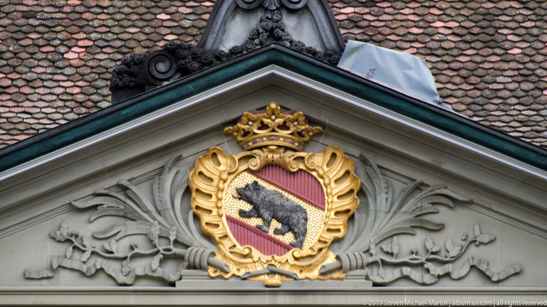 Gilded Bern coat of arms set in an ornate pediment below a red-tiled roof.
