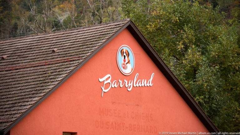Close view of a red tiled gable with the Barryland name, Saint Bernard dog emblem, and faint museum lettering.