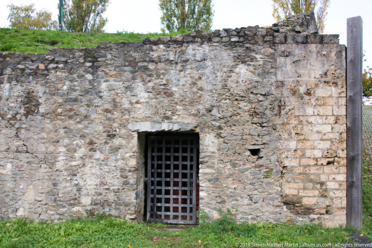 Close view of a barred rectangular doorway set into rough ancient stone masonry with larger cut stones at one side.