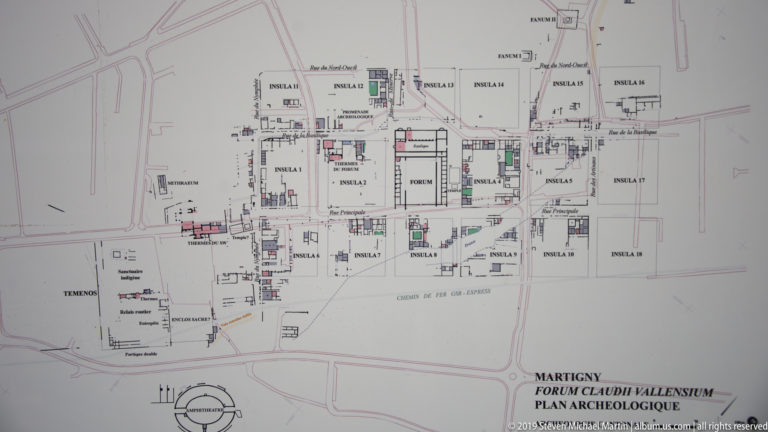 Printed archaeological plan labeled Forum Claudii Vallensium, showing insulae, streets, structures, and modern roads.