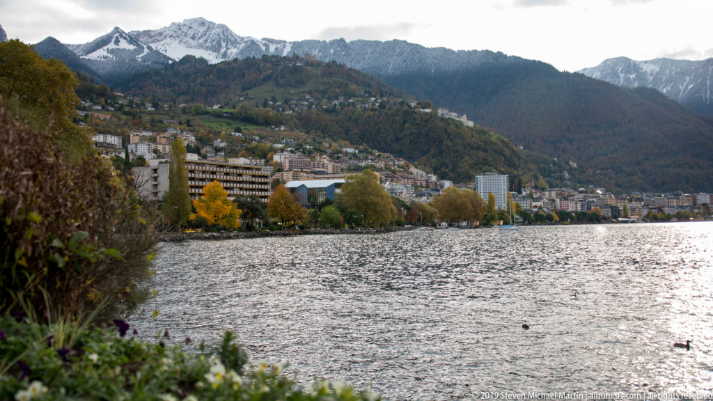 Lake Geneva beside Montreux’s autumn-lined waterfront, with hotels and homes climbing the wooded hillside.
