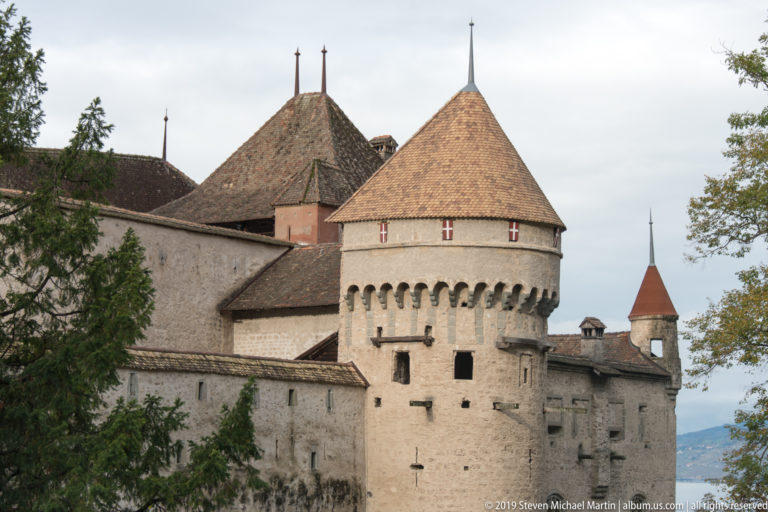 Large round stone tower with conical roof and projecting defensive masonry at Château de Chillon.