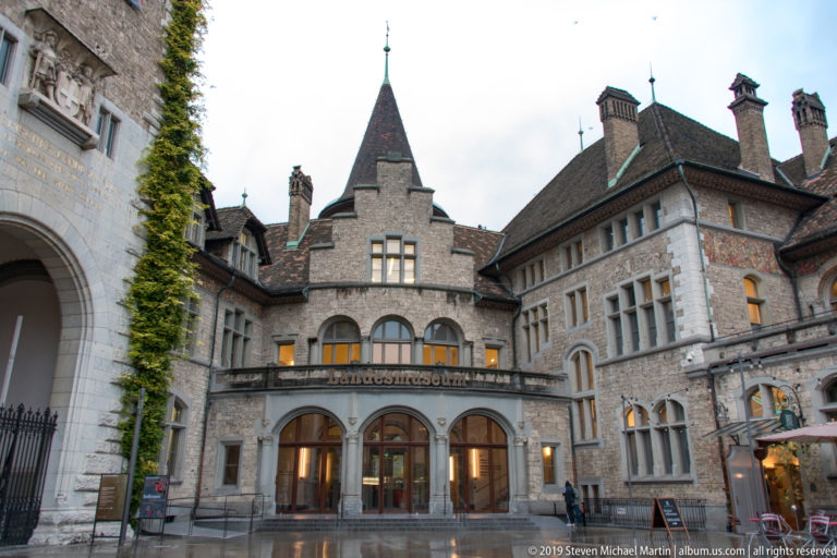 Historic Swiss National Museum entrance with rough stone walls, steep roofs, chimneys, arched openings, and wet forecourt.