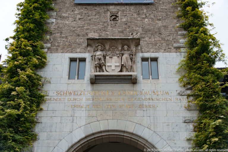 Stone entrance of the Swiss National Museum with Swiss-cross relief, German inscription, and ivy on both sides.