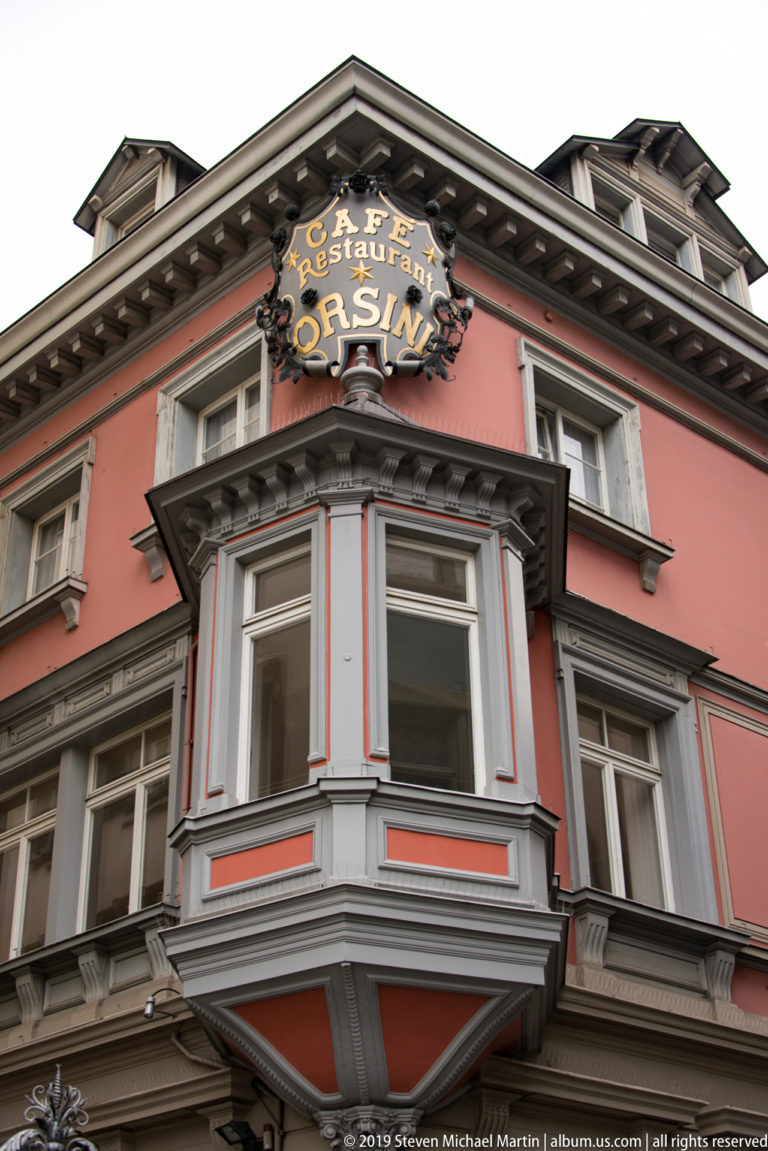 Salmon-colored Restaurant Orsini façade with gray projecting bay window and ornate sign near the roofline.