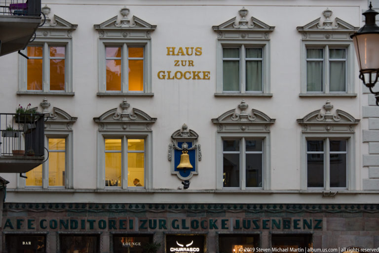 Haus zur Glocke façade with gilded name, blue shield bearing a bell, ornate windows, and café lettering below.