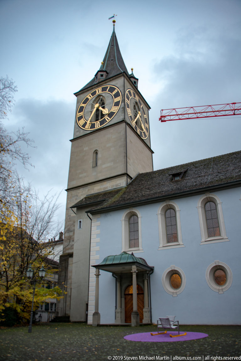 St. Peter Church in Zurich with large black-and-gold clock faces on its square tower above the pale nave.