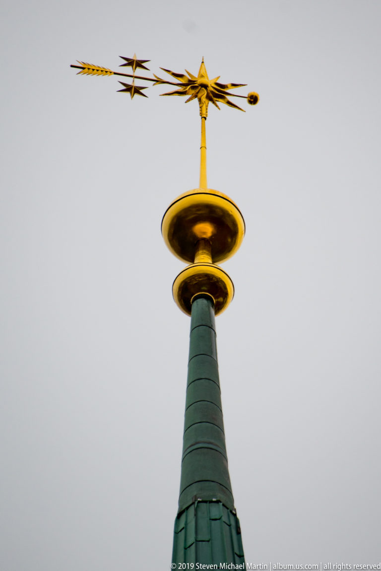 Gilded weather vane and star finial crowning the green copper spire of St. Peter’s Church in Zurich.