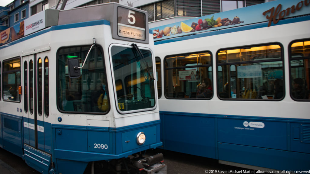 Two blue-and-white Zurich trams passing closely, with fleet number 2090 and route 5 to Kirche Fluntern visible.