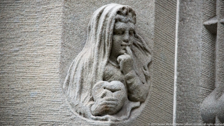 Small stone relief of a long-haired woman holding a child in a shallow architectural niche.