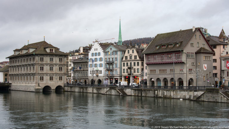 Zürich Rathaus beside a row of narrow historic buildings lining the Limmat waterfront.