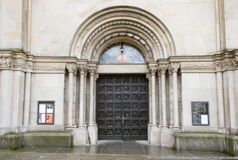 Round-arched Grossmünster portal with multiple stone archivolts, slender columns, dark paneled doors, and decorated tympanum.