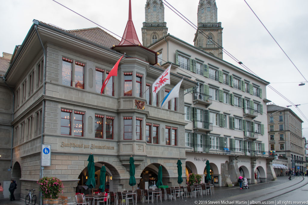 Zunfthaus zur Zimmerleuten with flags and arcades, with the twin Grossmünster towers rising behind.